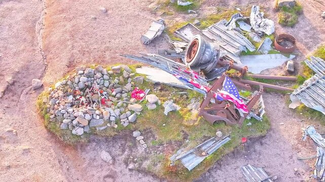 Drone rising over memorial B-29 Superfortress WWII plane wreckage site in the Peak District, England, waving US flag and stone grave in view.