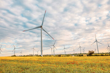Wind turbines are producing sustainable energy in a countryside field, set against a backdrop of a...