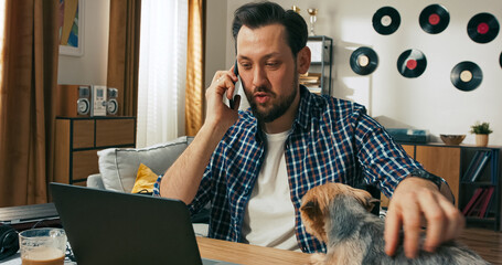 A relaxed person with a disability talks on the phone while working online, gently stroking a...