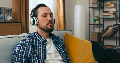 A middle-aged man enjoys an afternoon at home with music in his headphones, pausing as a friend sends a message about a friendly get-together, bringing a smile to his face.