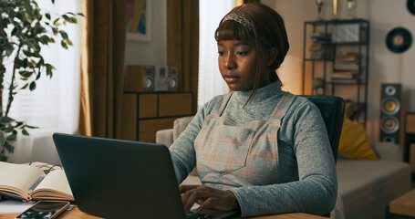 A professional woman is seated at her workstation, actively working on a laptop. She remains...