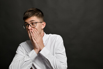  Surprised young man expresses psychological tension through pose. Hands at mouth suggest extreme...