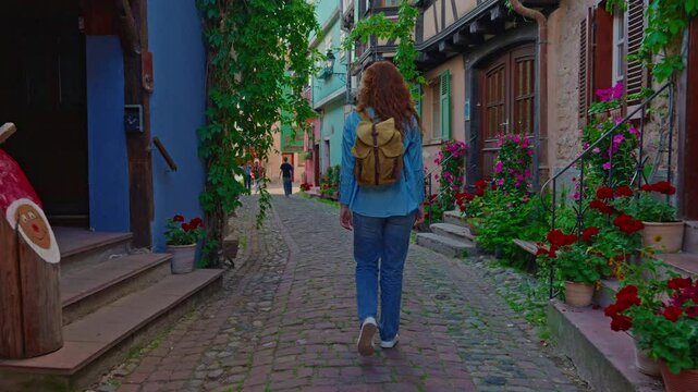 Woman with backpack walking on the beautiful street full of colorful houses with flowers of Eguisheim, France 