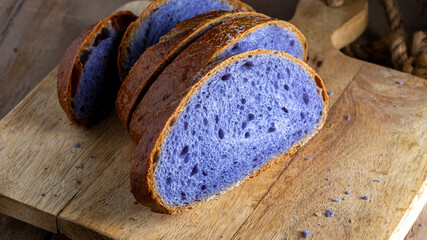 Slices of freshly baked purple bread cooked in blue Thai ancha tea sit on a rustic wooden cutting...