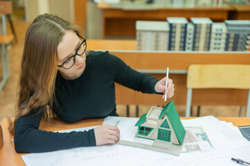 Caucasian young woman making a model of a building. Student of the construction university. 