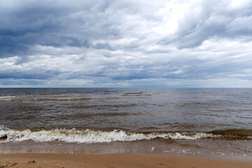 
A gloomy, cloudy day by the sea, where waves crash on a sandy shore.