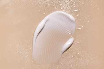 creamy white texture smear sample on light beige background with water drops close up