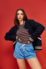 Stylish young woman showcases vibrant fashion against a bold red backdrop