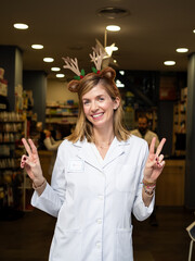 A cheerful female pharmacist poses at the entrance of her pharmacy wearing a festive Christmas...