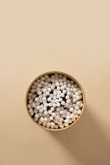 Wooden ecological cotton swab in paper container on beige background. Zero waste, sustainable resources. Close up. Vertical format.