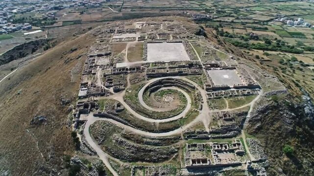 An aerial view showcases the ancient minoan palace of phaistos in crete, greece, with its distinctive spiral pathway and surrounding archaeological site