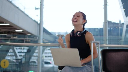 Young asian woman focused on her laptop computer in the airport, efficiently wrapping up work before her flight, She raised her hand in glee at the success of the event before boarding the plane.