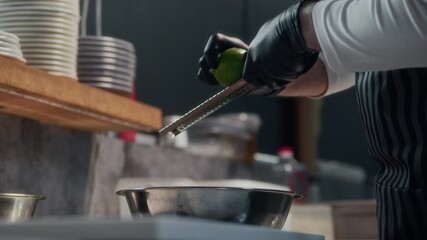 Cropped shot of gloved hands of unrecognizable chef grating lime zest over steel bowl in restaurant kitchen - Powered by Adobe