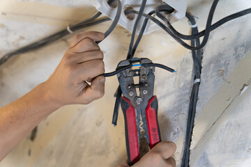 Electrician uses wire strippers to carefully remove insulation from an electrical wire, preparing...