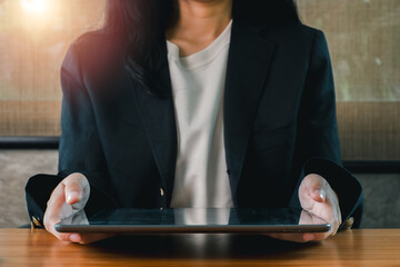 A business professional in a suit holding a tablet, sitting at a wooden desk with sunlight...