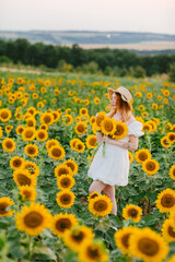Beautiful young girl in white dress and hat in sunflower field in summer