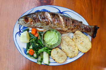 Wood oven roasted trout fish served with sauteed vegetables, green chutney and baked potatoes. Perfect family meal. Ideal for healthy eating and rustic food concepts. with copy space