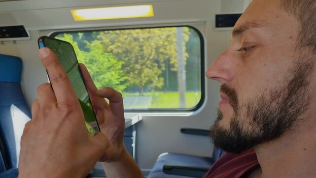 Close-up of a man's face and hands as he plays a mobile game while riding through lush spring landscapes on a high-speed Swiss train