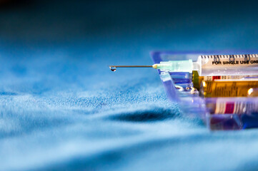 single-use medical syringe with medicine droplets and empty drug bottle indoors