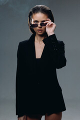 stylish woman wearing a black blazer and sunglasses poses confidently against a dark background...