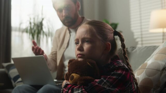 Caucasian family trouble at home father working online remote distant on couch with laptop ignoring angry talking to upset lonely daughter with toy child kid girl work life imbalance childhood sadness