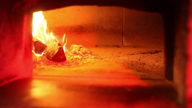 Traditional pizza being baked in a hot wood-fired oven while handled with a wooden pizza peel near the open flame.