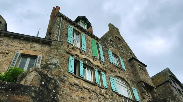 Old stone house with shuttered windows on a cloudy spring day in Mont Saint Michel Abbe, Normandy, France.