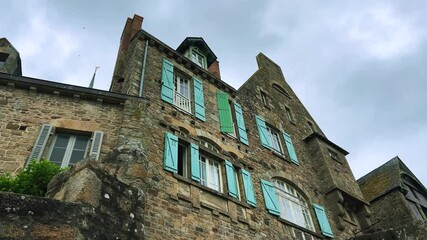 Old stone house with shuttered windows on a cloudy spring day in Mont Saint Michel Abbe, Normandy, France.