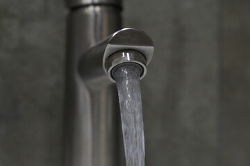 Clean water flowing from a brushed nickel faucet in a modern bathroom enhances a feeling of...