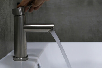 Opening a brushed metal faucet above a pristine white sink, a hand directs a stream of fresh water...