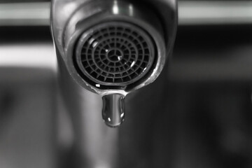 Close-up of a dripping faucet in monochrome, highlighting water waste, conservation, and plumbing...