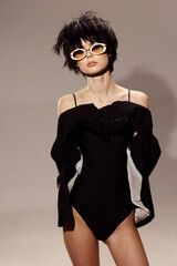 young woman posing confidently in black off-shoulder bodysuit with white sunglasses, short dark...