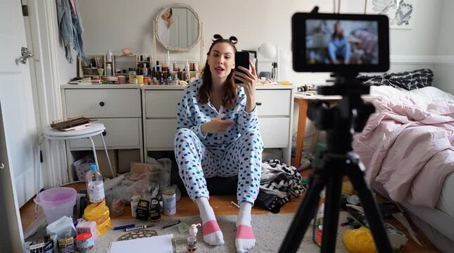 Young female influencer recording a GRWM (Get Ready With Me) video for social media, sitting on the floor and talking to her phone camera.

