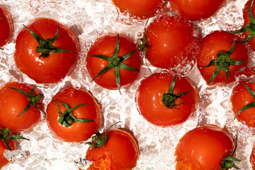 Vegetable background of fresh whole tomatoes in water, splash of water, top view.