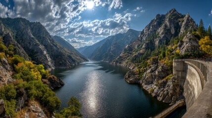 A wide-angle view of a dam and its reservoir, showcasing the natural landscape, with mountains in the background and the water glistening in the sunlight