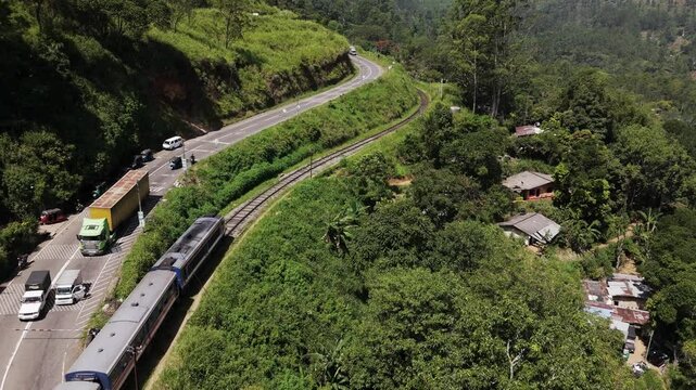 Train travels along tracks beside road in picturesque hillsides of Sri Lanka on this iconic journey. Drone aerial follow.