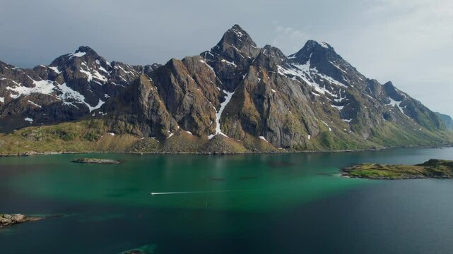 Breathtaking aerial view of a boat sailing on the turquoise waters of the Steinsfjorden, with the snow capped peaks of the Lofoten Islands in the background