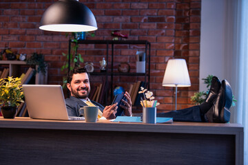 Feet on desk, Indian professional uses tablet, representing relaxed modern business lifestyle
