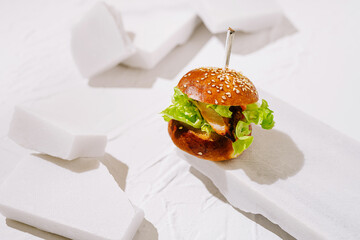 Mini burger with lettuce on a white surface decorated with foam pieces