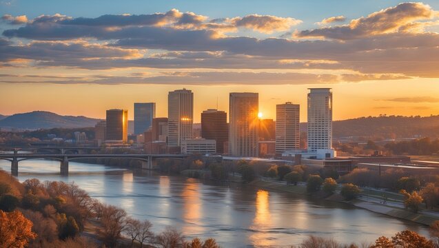 Displaying high-rise city skyline glowing at sunset over river, with multi-span bridge and trees