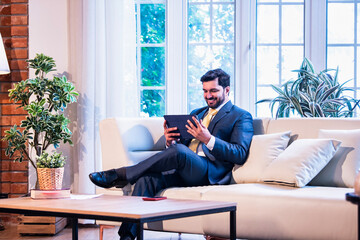Businessman with tablet on couch in office, symbol of confidence, technology, and smart working