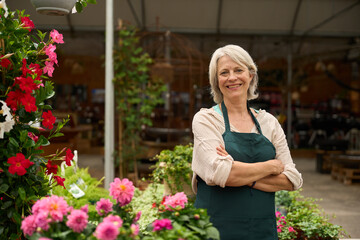 Senior florist smiling with crossed arms in flower shop
