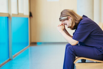 Exhausted nurse feeling stressed sitting in hospital corridor