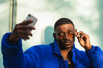 Portrait of trendy cool black man with sunglasses taking a selfie with his cell phone