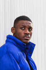 Side view of confident African American male model wearing vivid blue jacket while standing on...