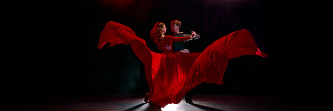 A vibrant pair elegantly executes a passionate Argentine tango under striking red illumination. Concept of intense romance and showcases skilled dance movements. Banner
