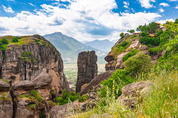 View of dramatic Meteora rock formations and distant village from grassy cliffside in Meteora Greece