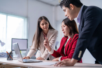 Three people are sitting at a desk, one of them holding a pen