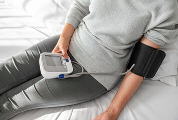 A person checks their blood pressure using a digital monitor while sitting indoors, highlighting a...