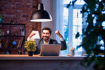Indian businessman celebrates success at work with laptop, expressing victory and happiness